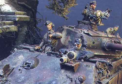 The Panther crew takes a look about.  The Sturmmann radio operator is a Warriors figurine in a Plane Tree no.  pattern coverall, puts a pack of fags back into his pocket whilst gazing at the IR carrying grenadier on the meadow above. The Sturmmann driver beside him is a combination of a Verlinden body and left arm with a Jaguar head and left arm. Note the Panther's front plate covered with shell impacts. The bow mg plug is from Aber's photo-etch set. Also note the sheared mantlet from a glancing blow.